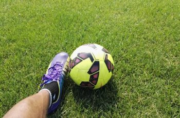 Balón de fútbol junto al pie de un futbolista en el campo de juego.