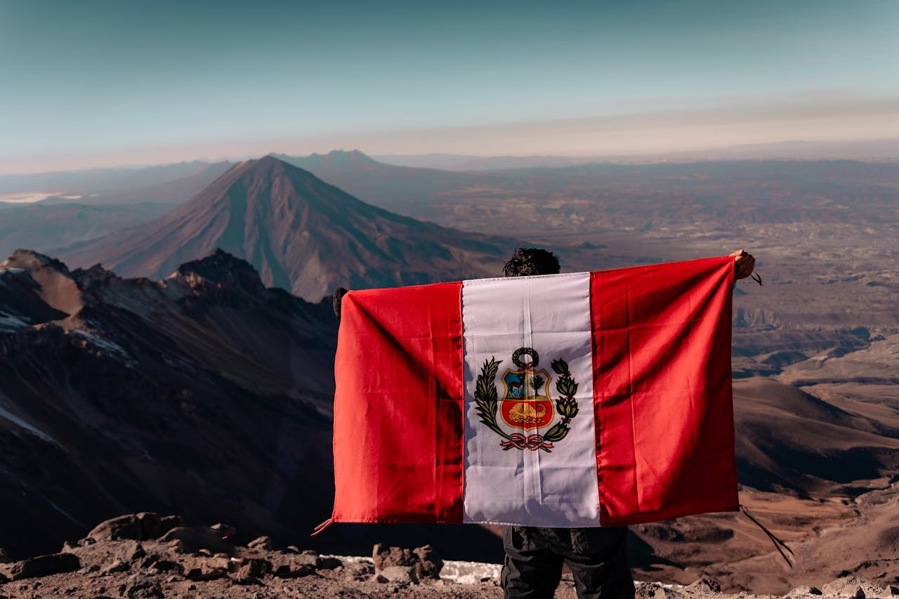 Hombre con la bandera de Perú en la espalda en la cima de un monte.