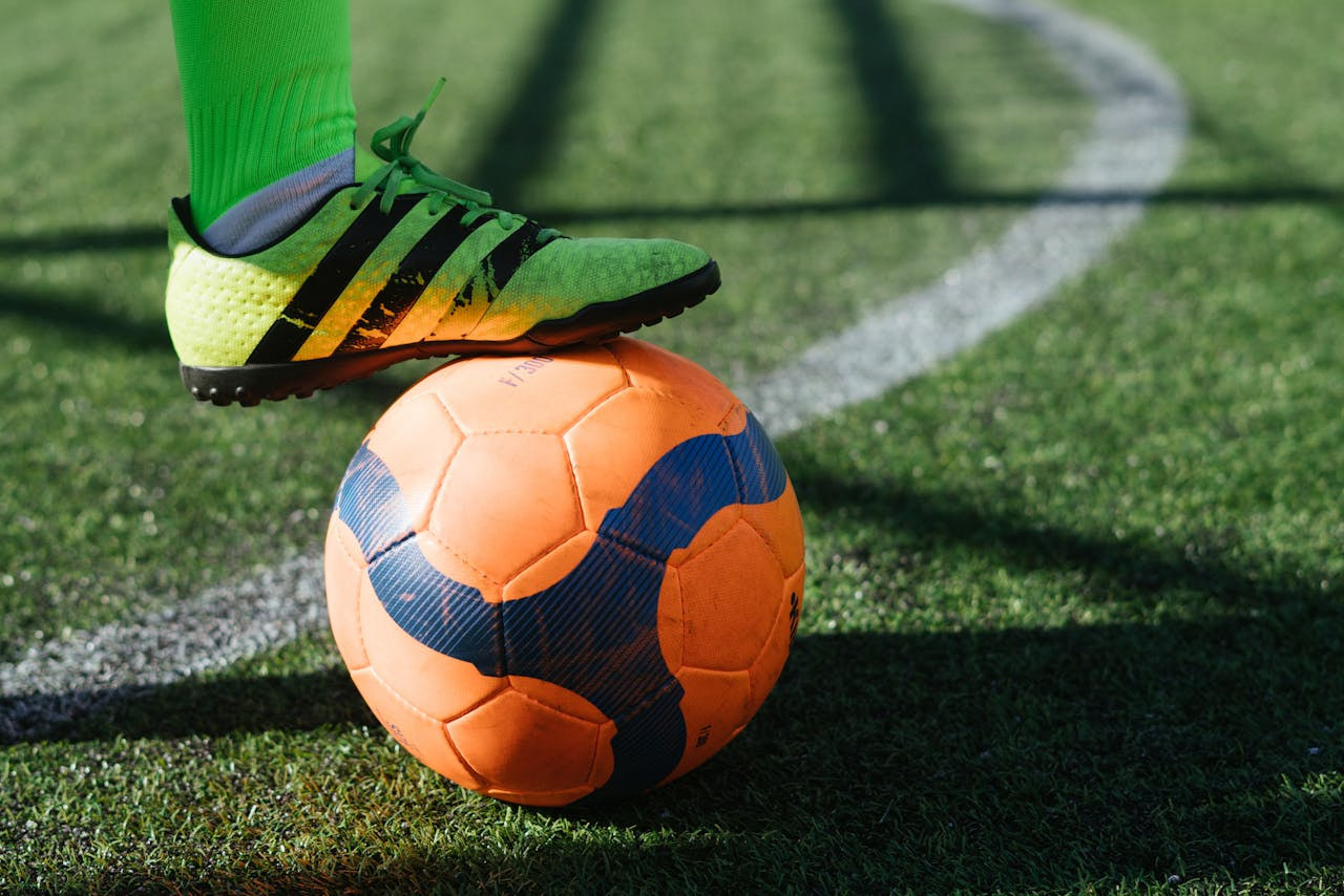 Pie de un futbolista pisando un balón sobre el césped de un campo de fútbol.