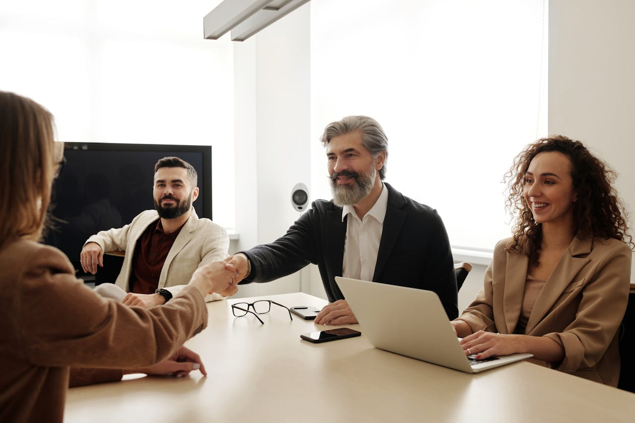 Dos personas estrechándose las manos en una mesa de reuniones acompañadas por otras dos.