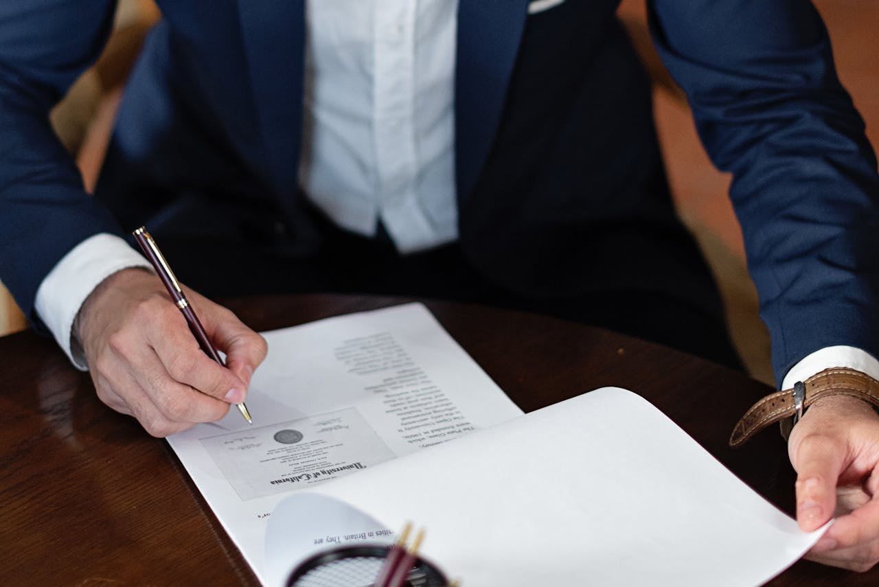 Hombre en traje firmando un pliego de papeles sobre una mesa.