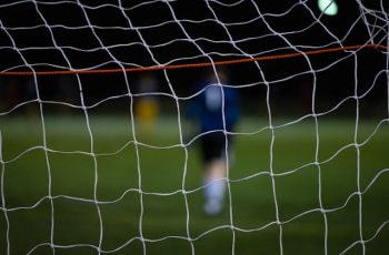 Red de una portería de fútbol con el portero difuminado al fondo.