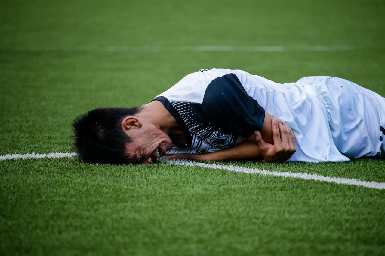 Futbolista con gesto de dolor tumbado bocabajo sobre el césped del campo.