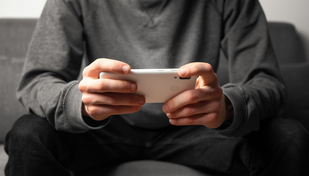 Hombre jugando con su teléfono sentado en un sofa.