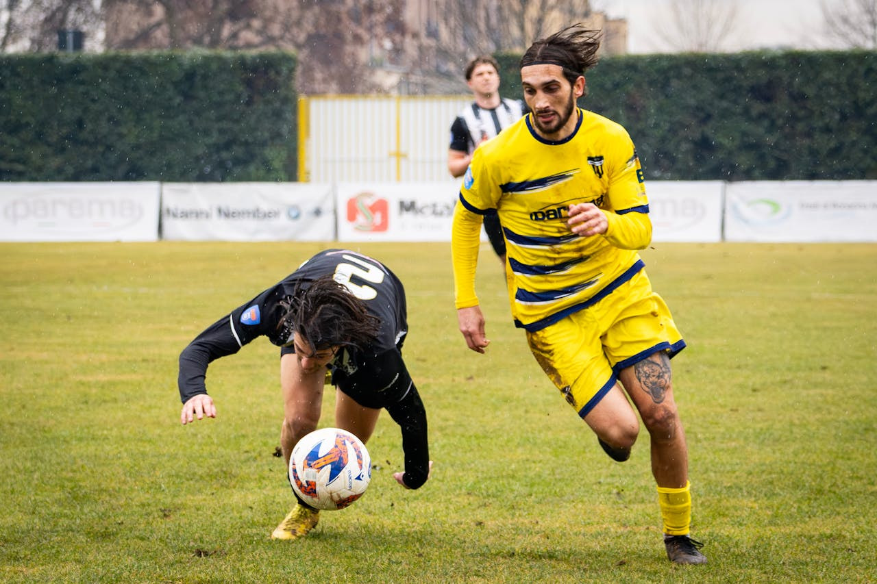 Dos jugadores corriendo detrás del balón en un partido de fútbol.