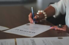 Mujer firmando un diploma sobre una mesa.